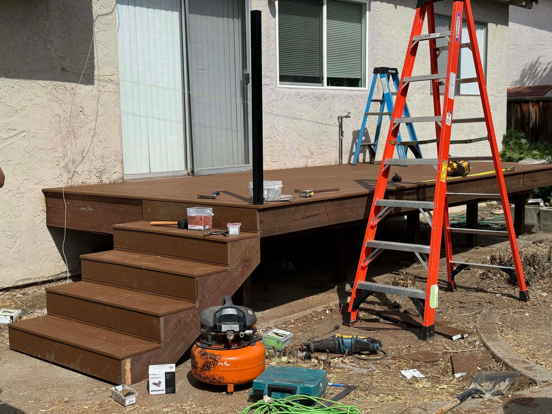 Patio with brown pergola and clear roofing over wicker chairs. Wooden fence and siding in background.