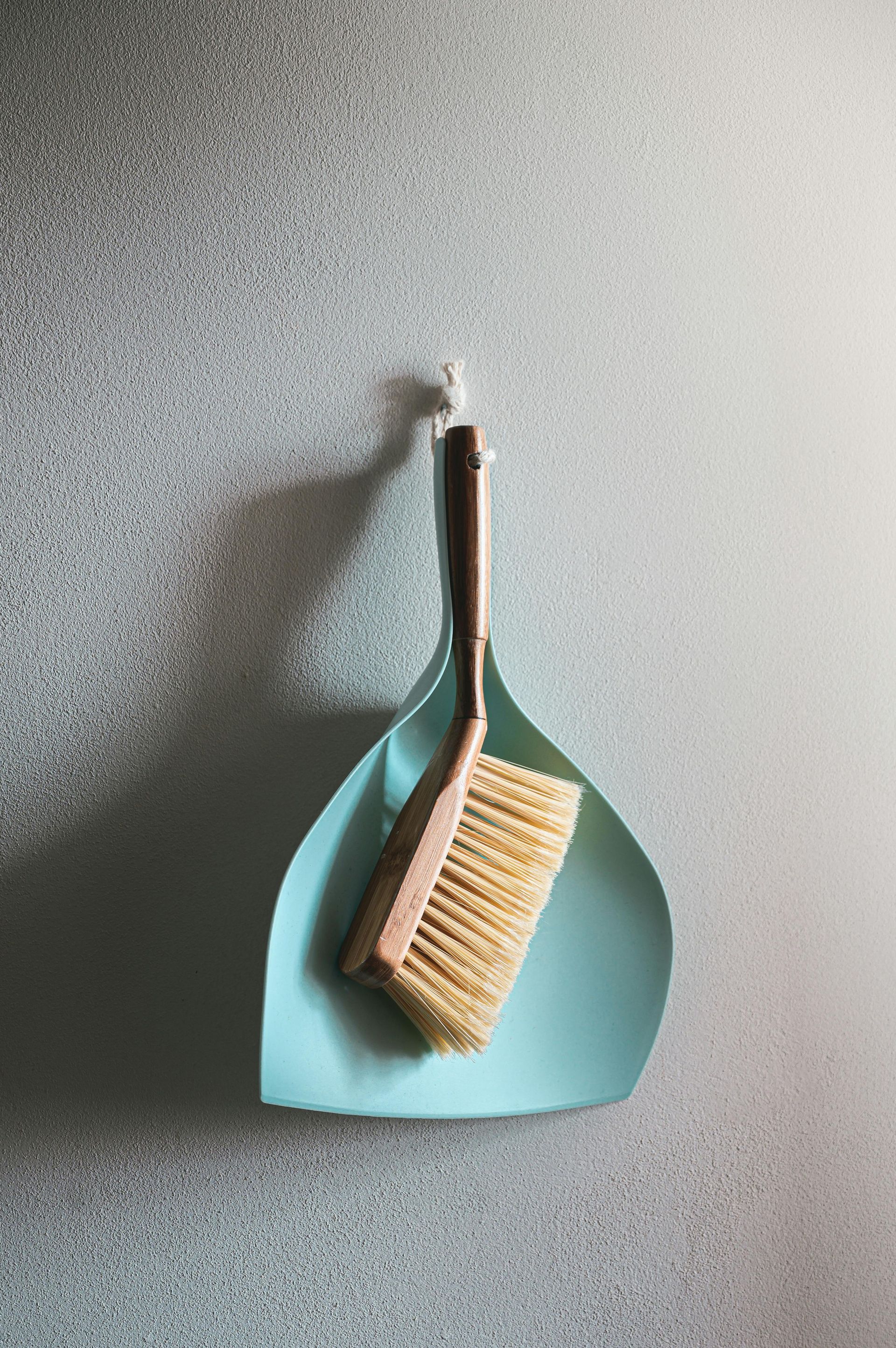 A brush and scoop are hanging on a hook on a wall.