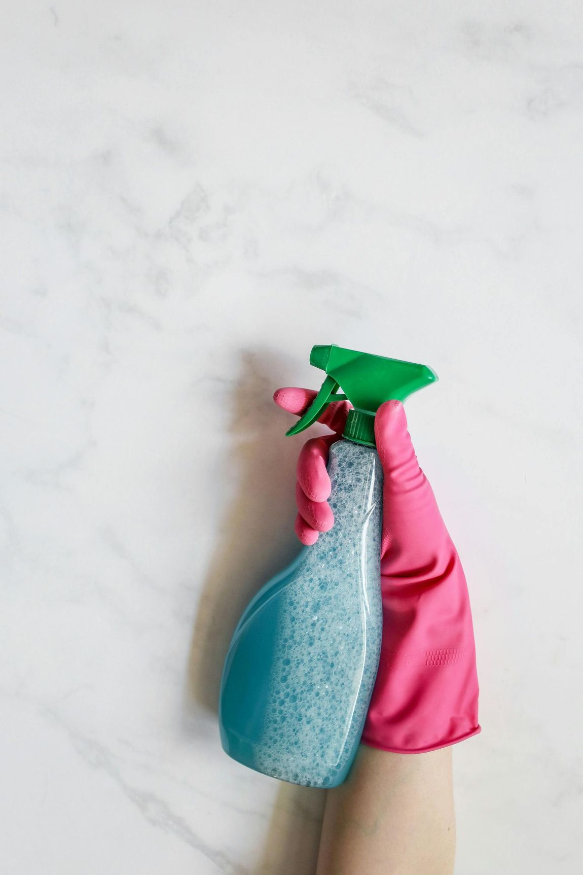 A person wearing pink gloves is holding a spray bottle and a sponge.