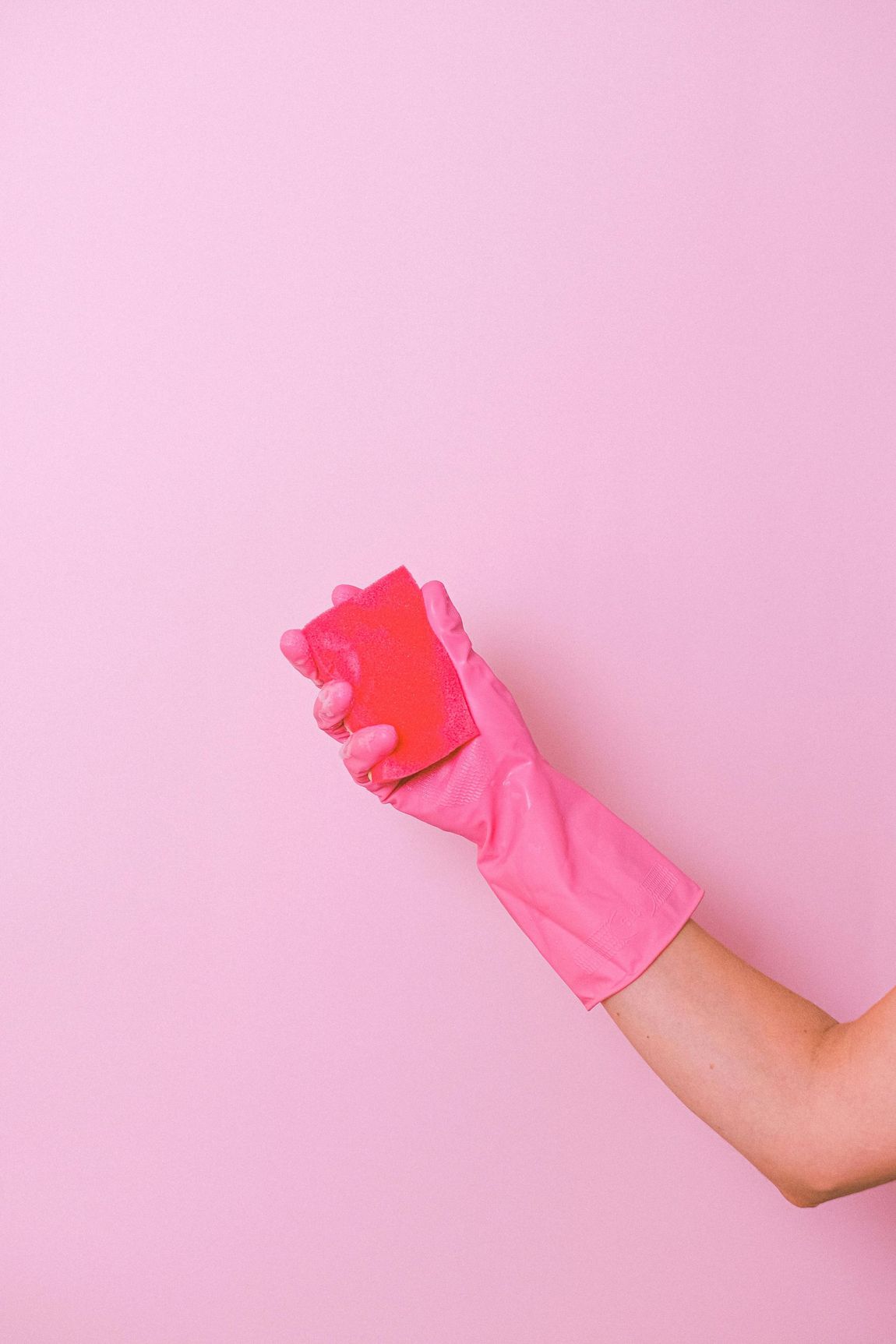 A woman is wearing a pink glove and holding a red sponge.