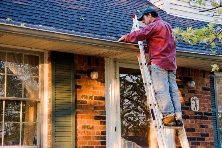 Worker on a ladder painting the roofline of a brick house