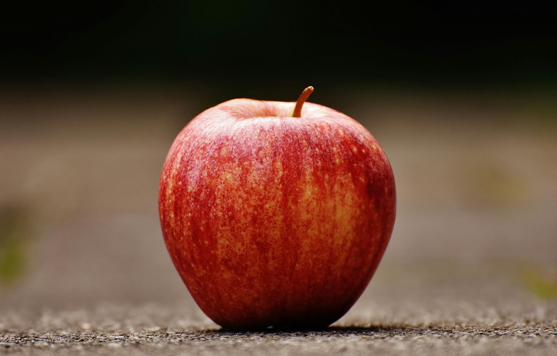 A single red apple is sitting on the ground.