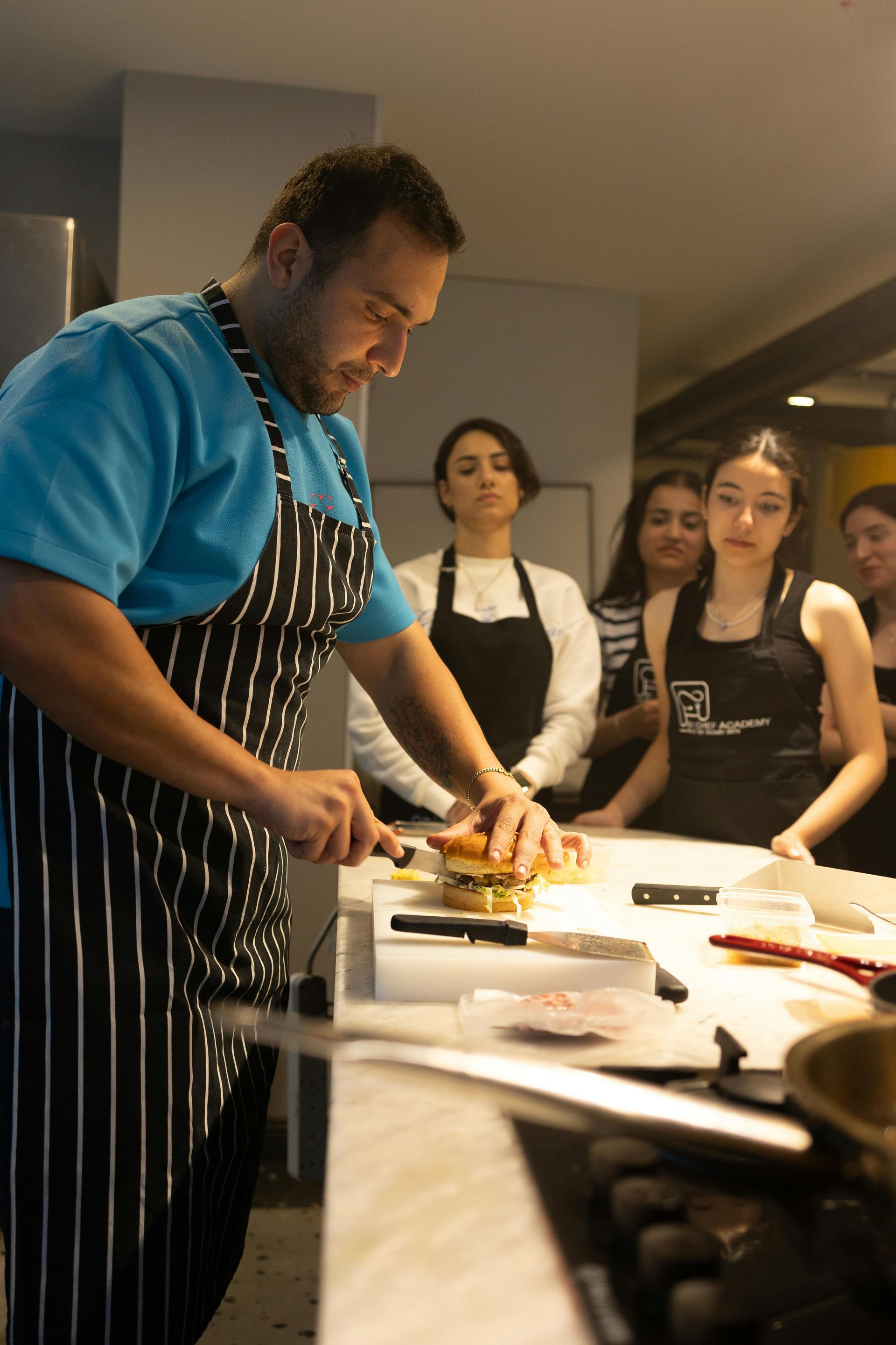 A man in an apron is cutting a hamburger in front of a group of people.