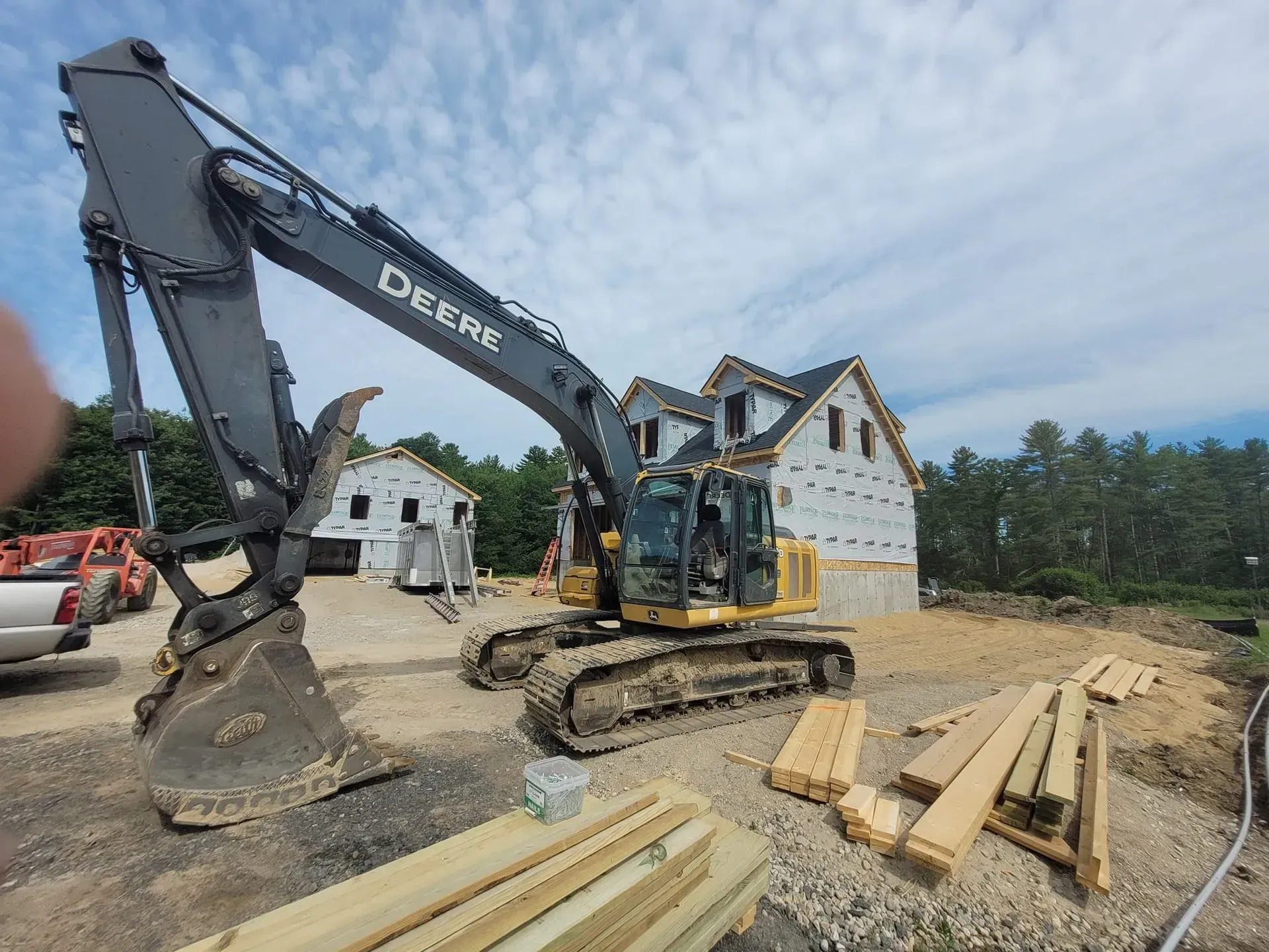 A large excavator is sitting in front of a house under construction.