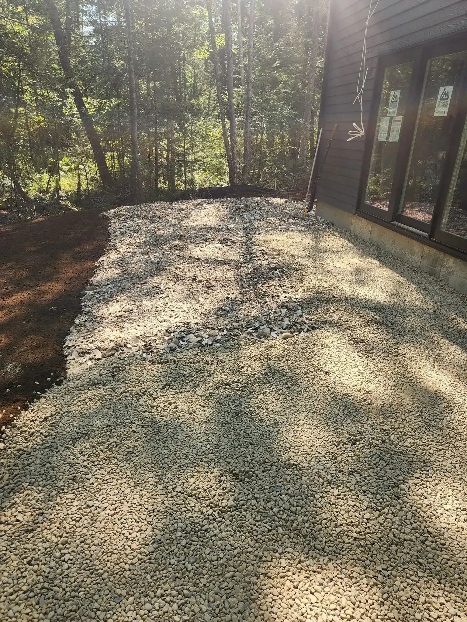 Gravel pathway beside a building with large windows. Trees in the background, sunlight.