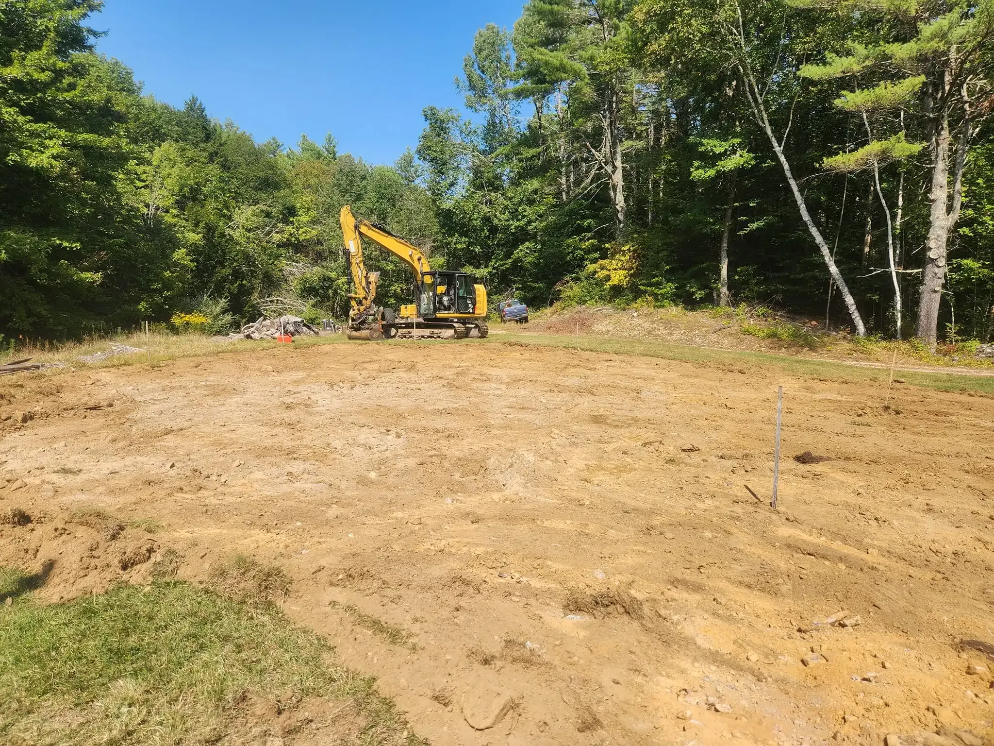 A yellow excavator is working on a dirt field surrounded by trees.