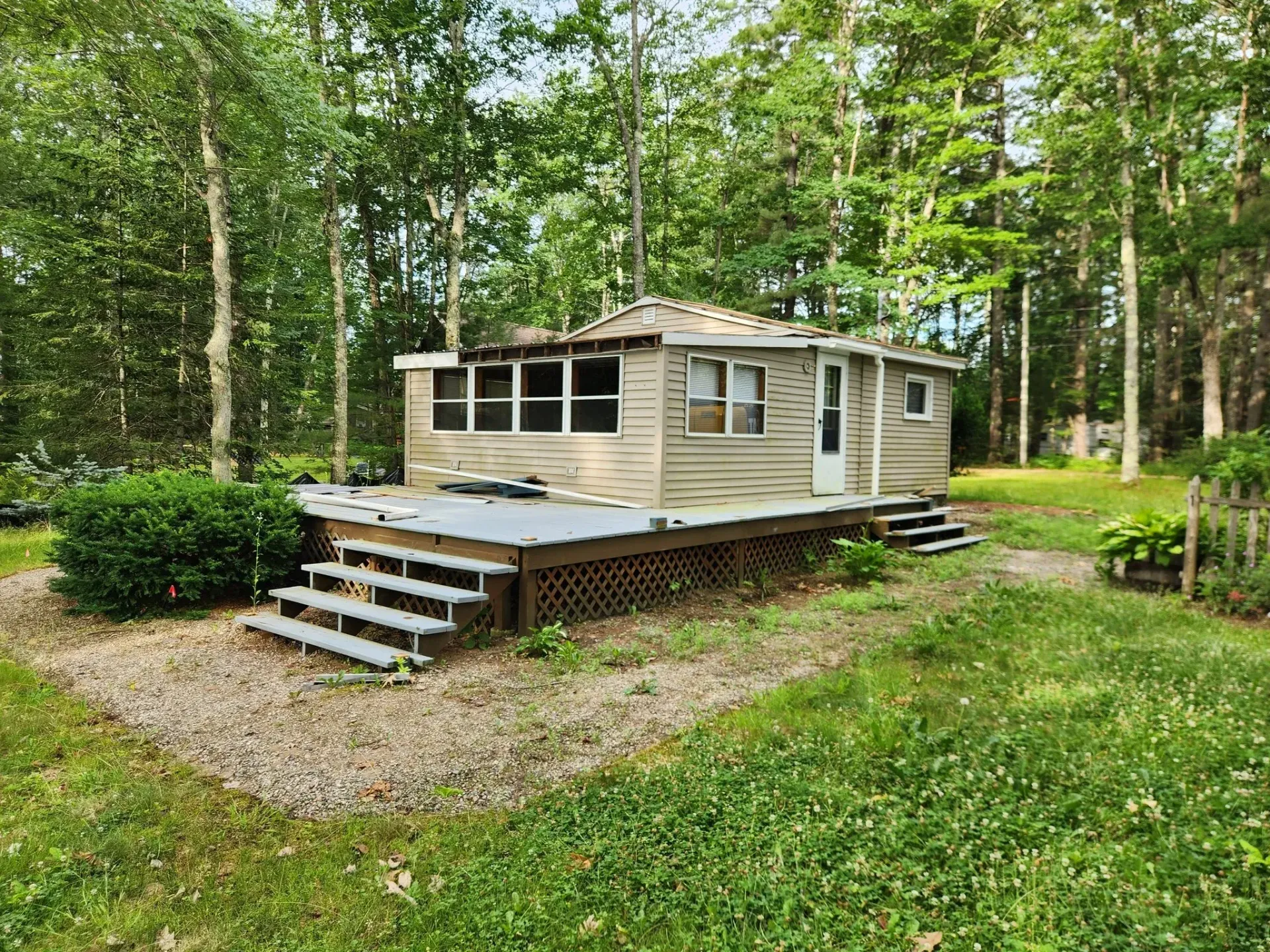 Small cabin with a deck, surrounded by trees and grass.