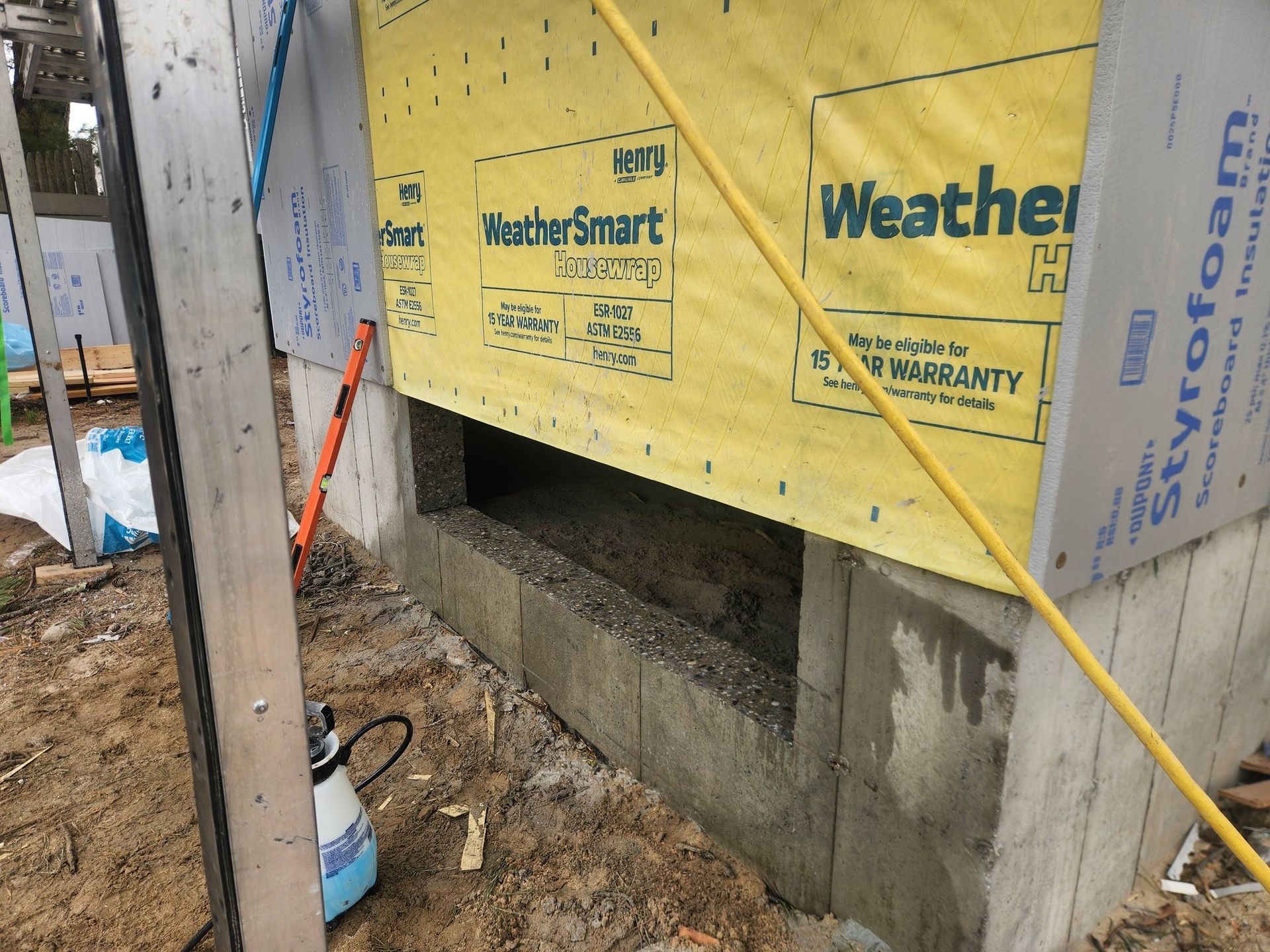 Construction site showing a gap in a cinder block foundation wall beneath yellow house wrap and Styrofoam insulation.