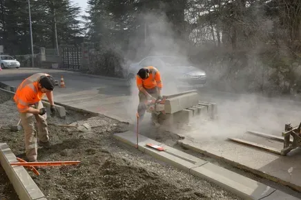 Two construction workers are cutting concrete with a circular saw.