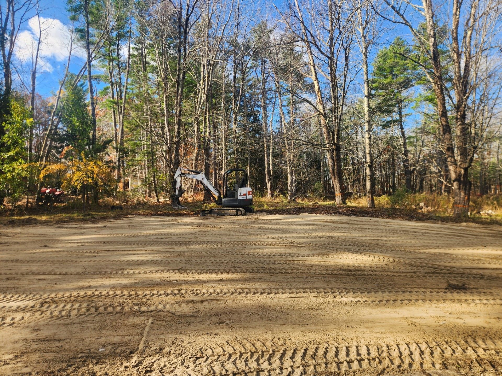 Construction site with an excavator on cleared land, surrounded by trees.