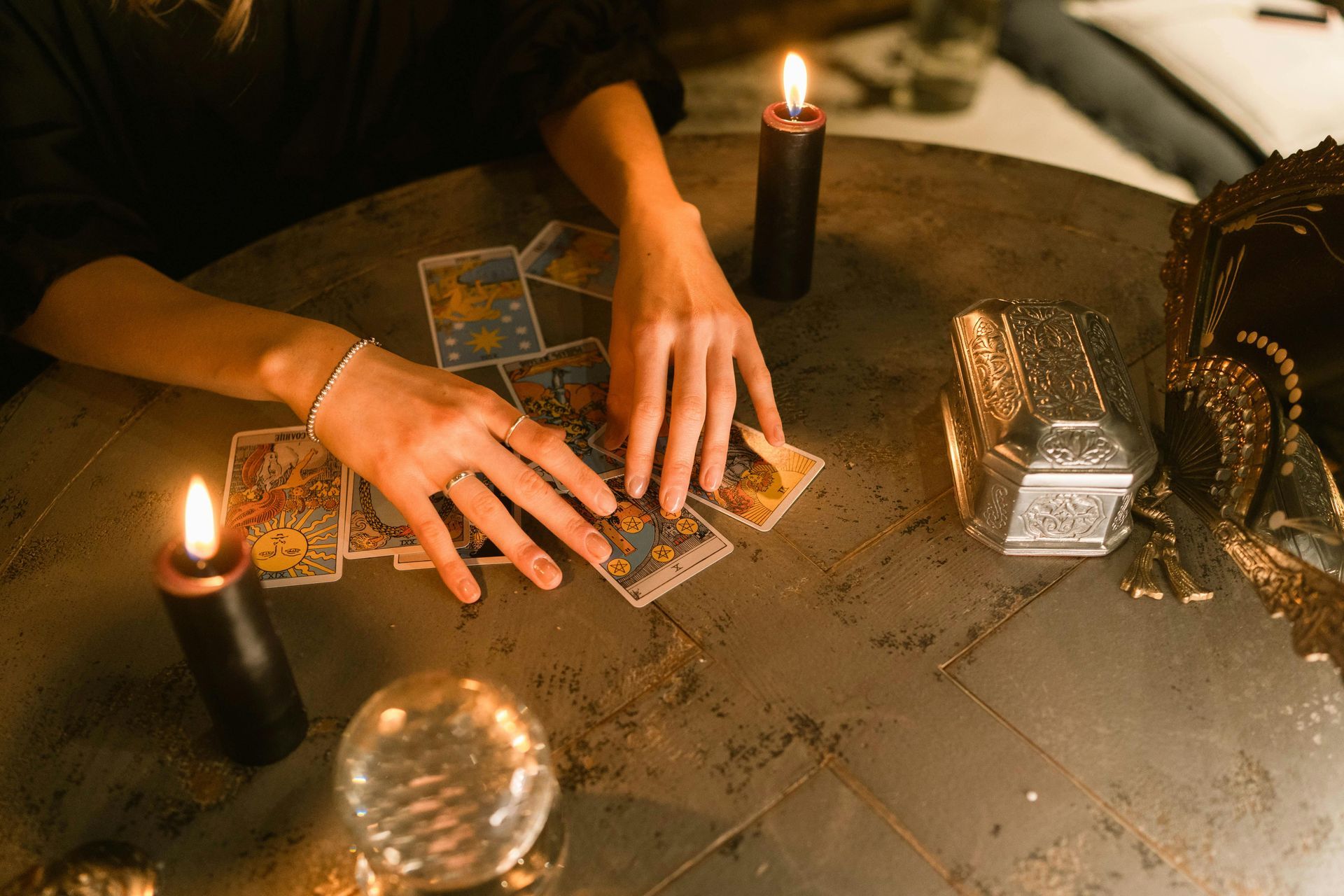 A woman is sitting at a table with candles and tarot cards.