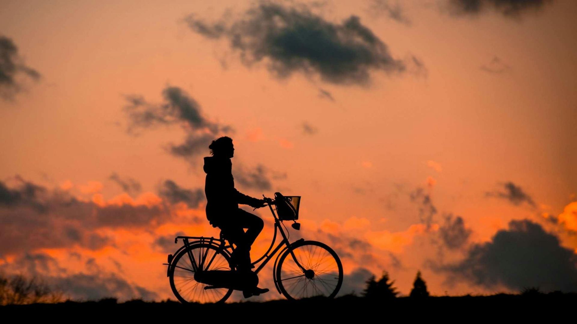 Silhouette of person on a bicycle against a vibrant orange and dark sunset with clouds.