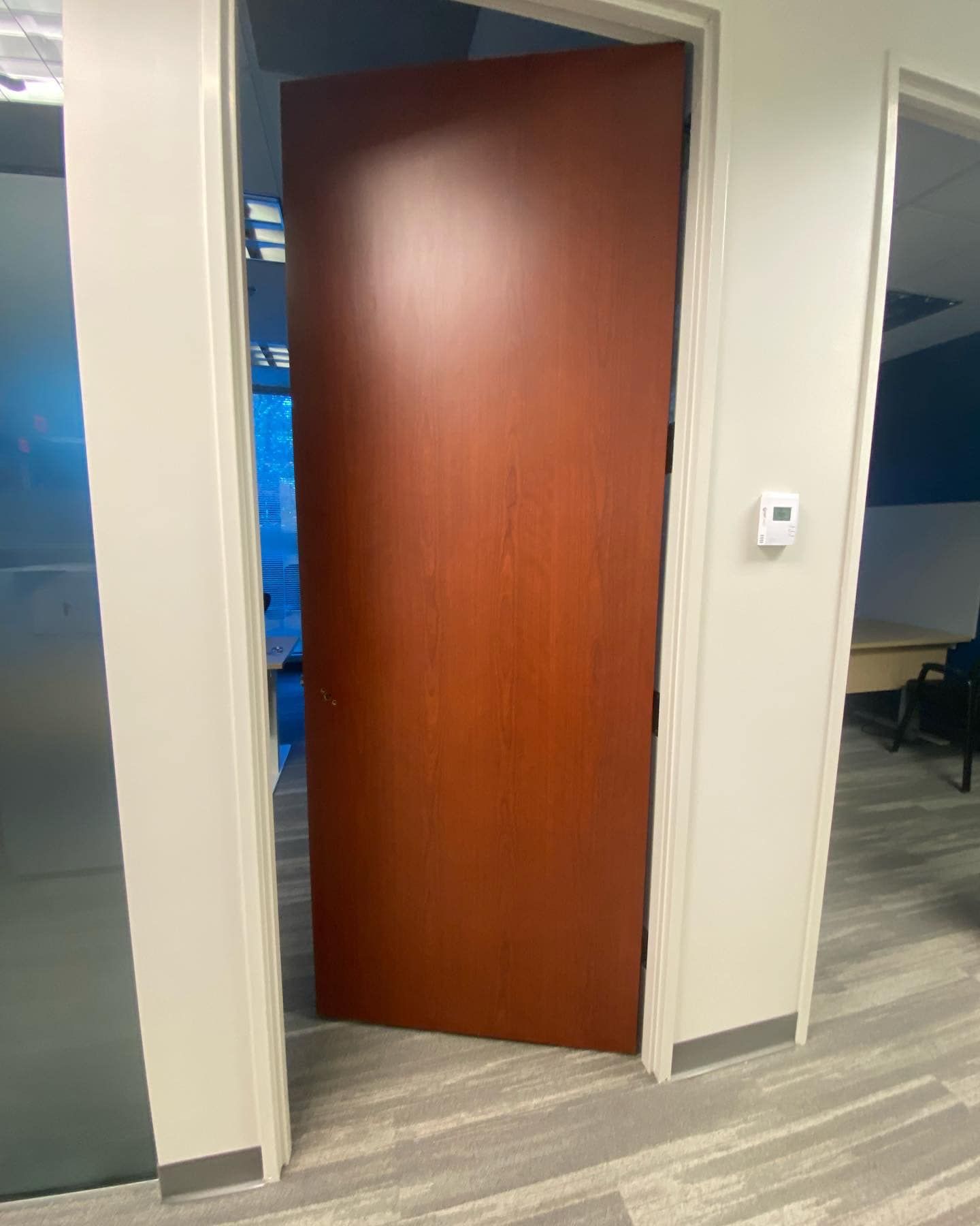 A wooden door is open in a hallway between two rooms.