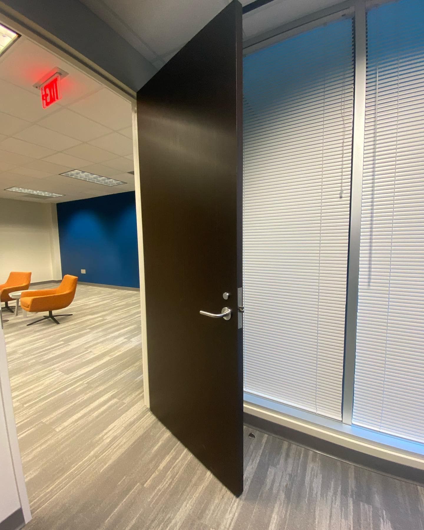 A door is open to a room with a red exit sign on the ceiling.