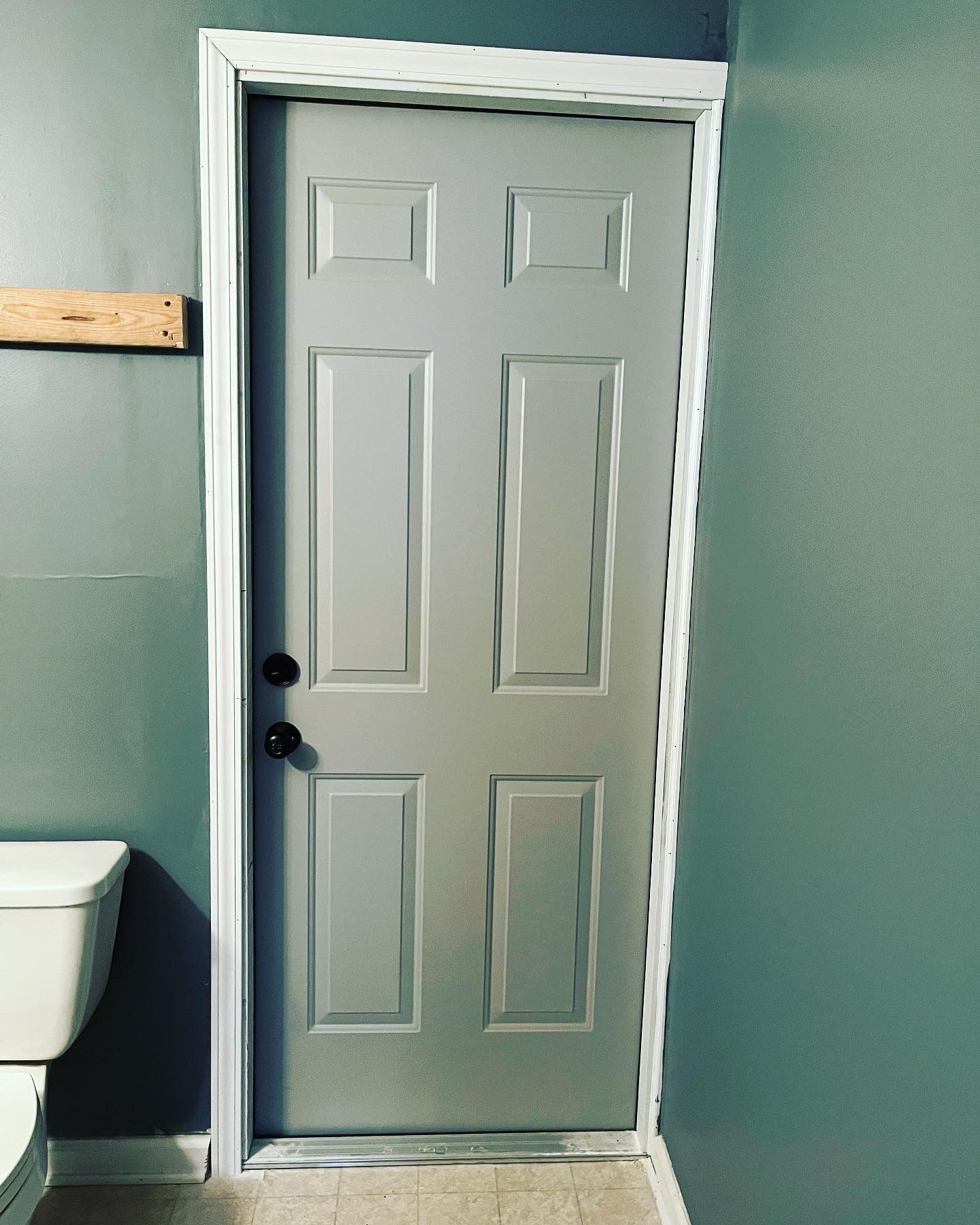 A gray door in a bathroom next to a toilet