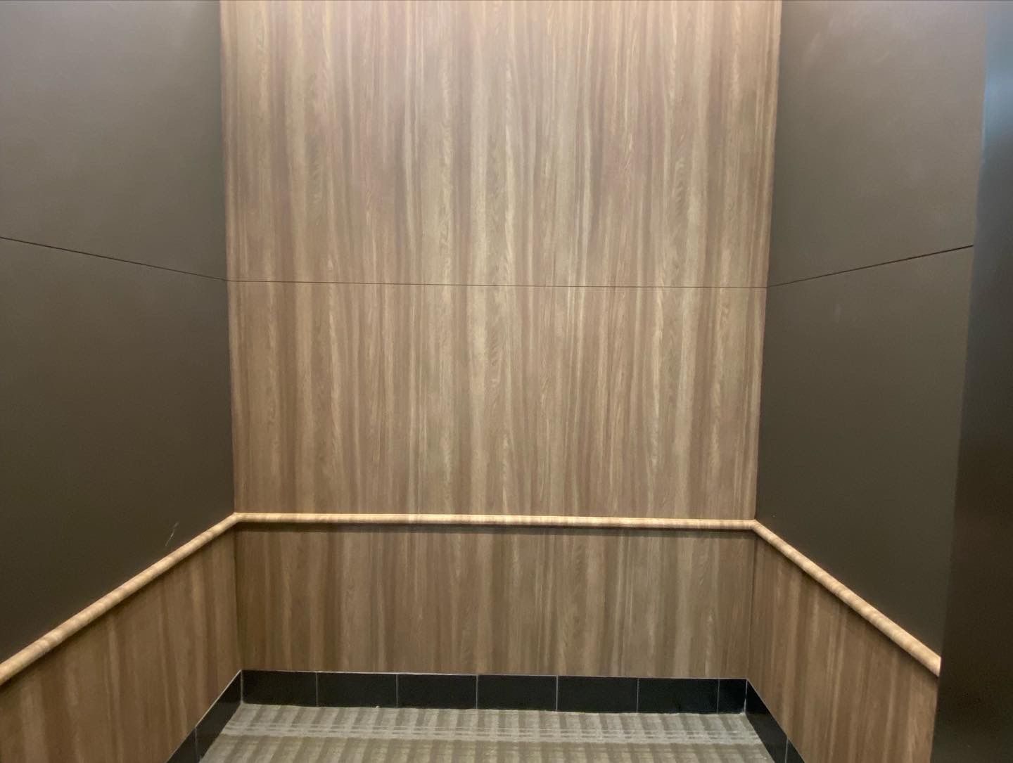 The inside of an elevator with wooden walls and a stainless steel railing.