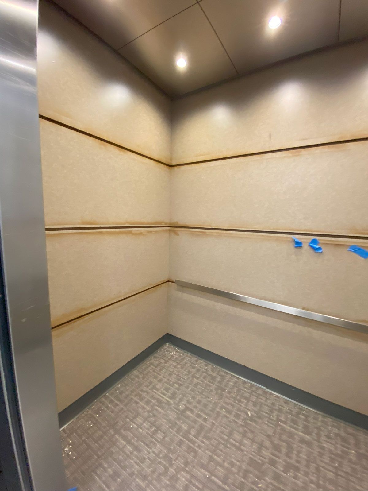 An empty elevator with a stainless steel wall and a tiled floor.