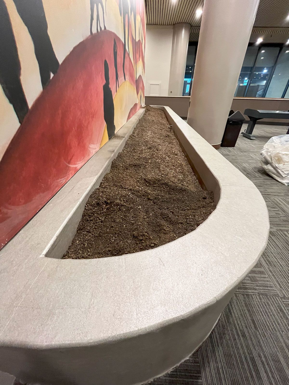 A large planter filled with dirt in a room with a painting on the wall.