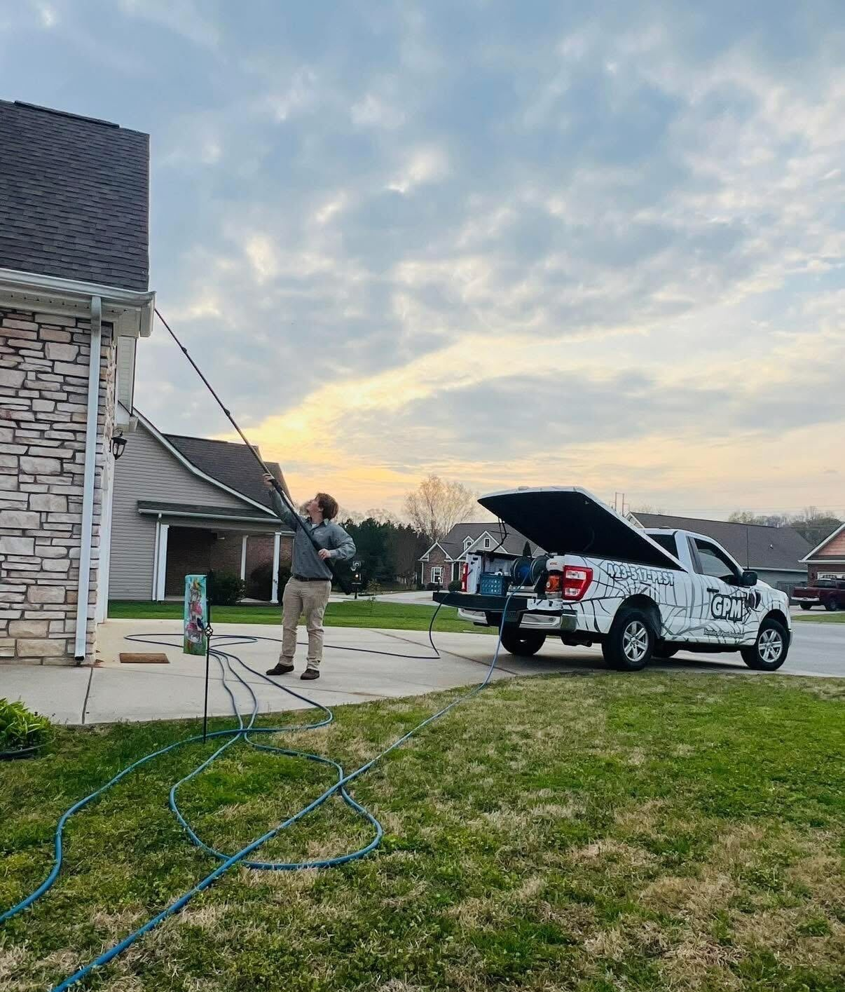 Person standing in driveway beside white SUV with open hood and a house in the background