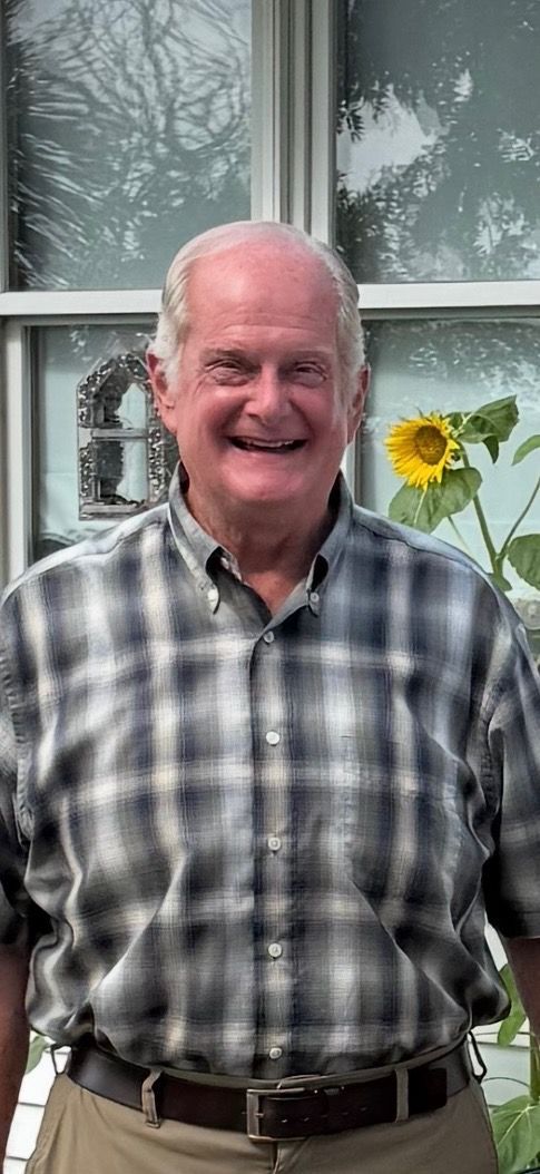 A man in a plaid shirt is standing in front of a tree.