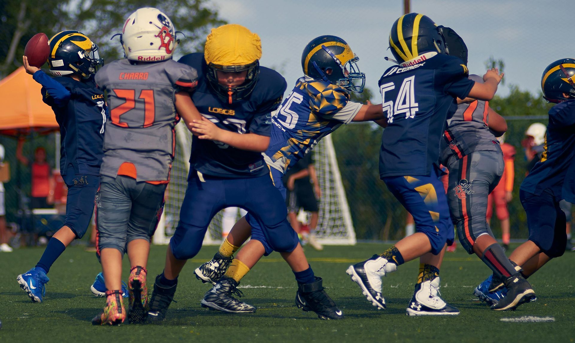 Youth football players in navy and gray uniforms clash during a game on a green field.