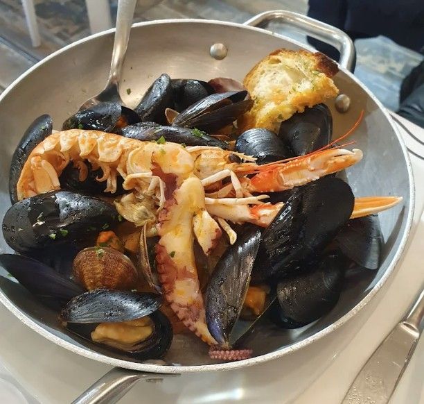 Stufato di pesce in una ciotola di metallo, con cozze, vongole, aragosta, polpo e pane tostato.