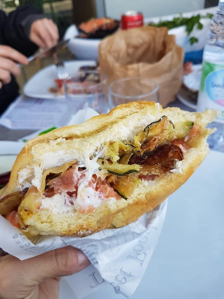 Mano che tiene un panino con verdure grigliate e salsa cremosa; all'aperto, a un tavolo.