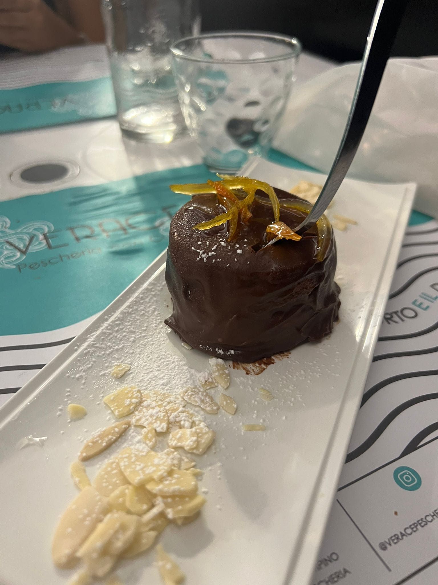 Dolce al cioccolato su un piatto bianco con lamelle di mandorle, zucchero a velo e una forchetta d'argento.