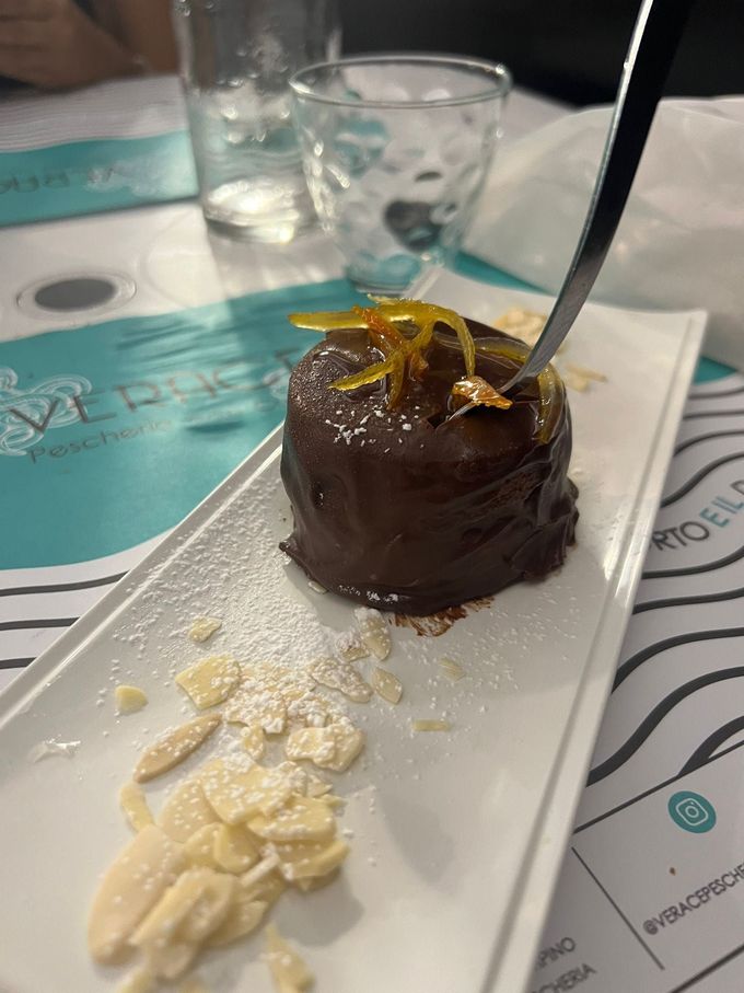 Dolce al cioccolato su un piatto bianco con lamelle di mandorle, zucchero a velo e una forchetta d'argento.