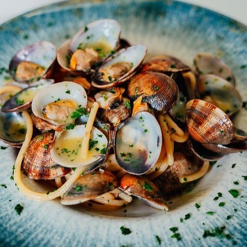 Pasta con le vongole in una ciotola blu, guarnita con prezzemolo.
