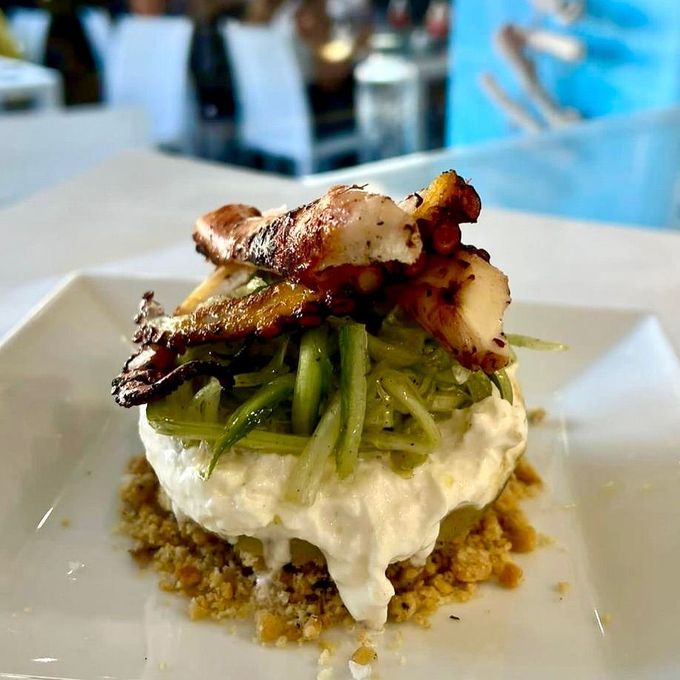 Polpo grigliato su un letto di verdure e salsa bianca cremosa, servito su un piatto quadrato.