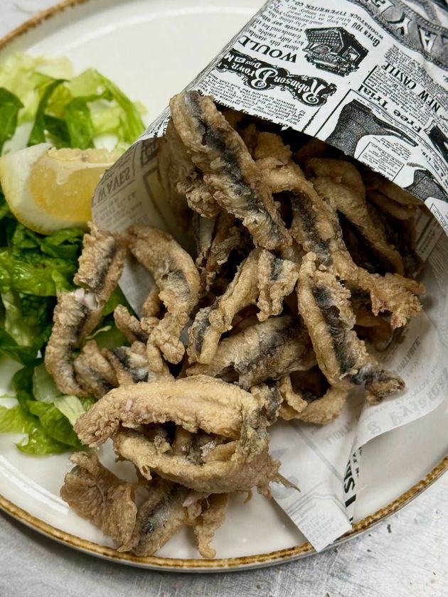 Pesce fritto in un cono di carta, servito con lattuga e spicchio di limone su un piatto.