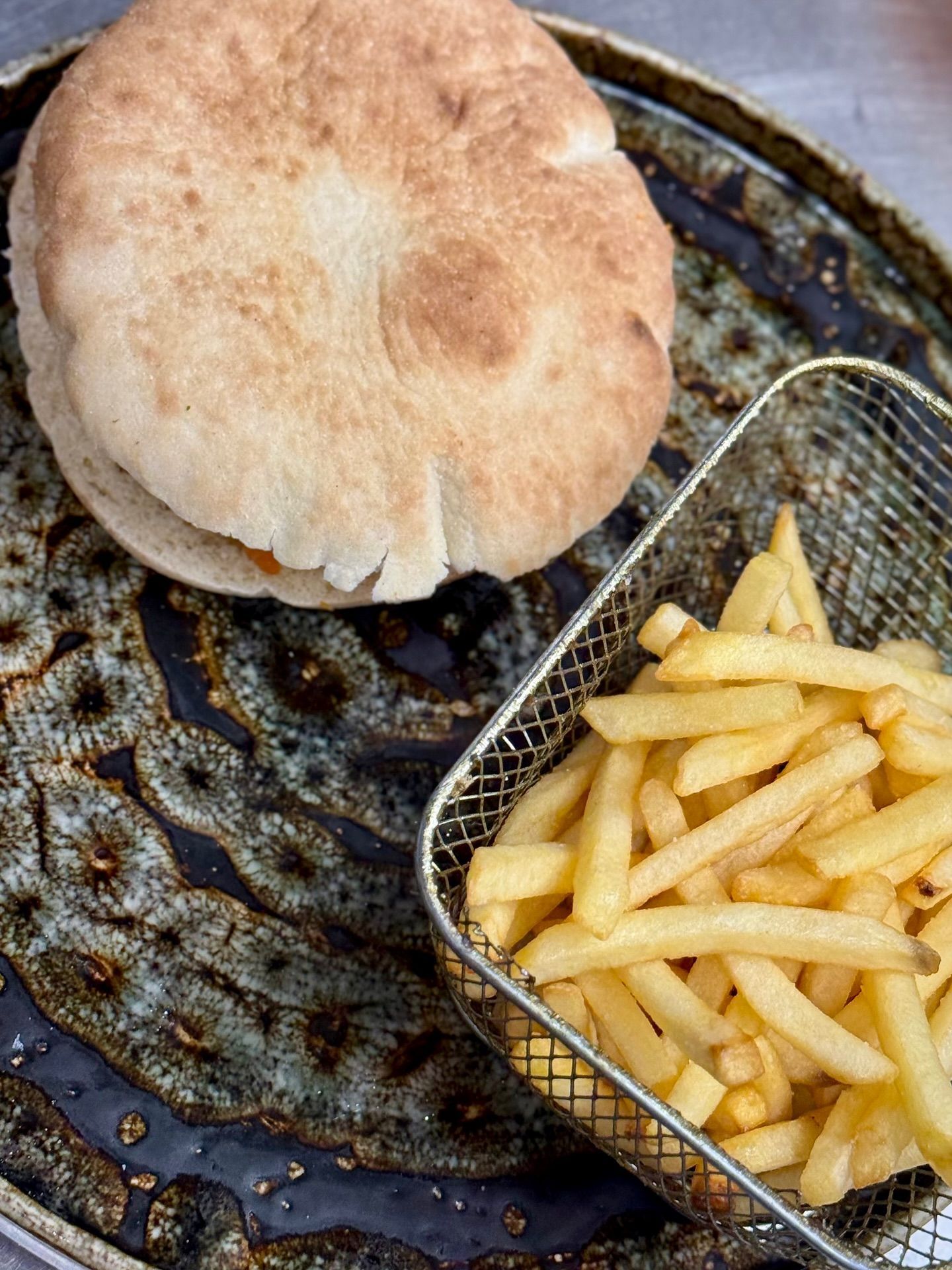 Panino pita su un piatto decorato accanto a un cestino di patatine fritte dorate.