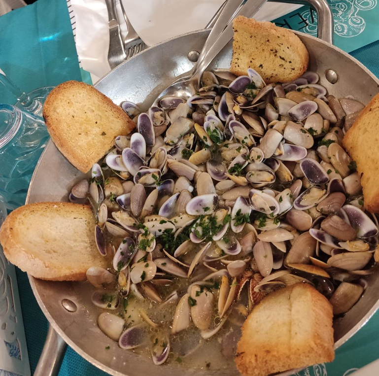 Vongole in padella con pane all'aglio, servite su un tavolo con una tovaglia blu.