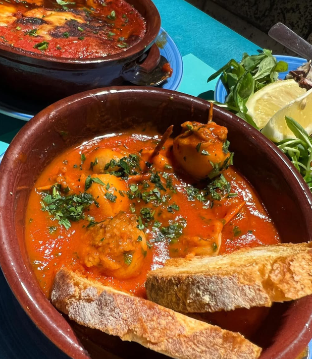 Frutti di mare stufati in salsa rossa, serviti in una ciotola marrone con pane tostato e guarnizione di prezzemolo.
