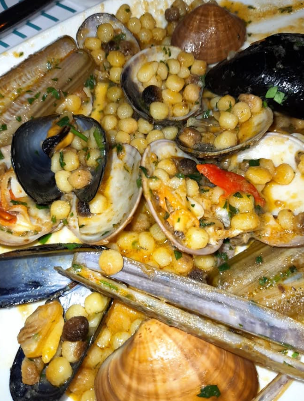 Piatto di frutti di mare con vongole, cozze e pasta, primo piano. Salsa marrone chiaro, guarnizione verde.