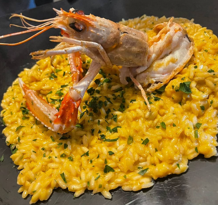 Risotto con un grande gambero, guarnito con prezzemolo su un piatto nero.