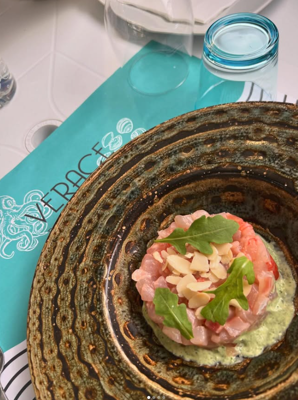 Primo piano di un piatto di pesce con un menu blu, su un piatto marrone testurizzato.