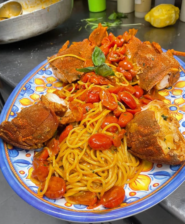 Spaghetti con aragosta, salsa rossa e pomodorini su un piatto decorativo blu e giallo.