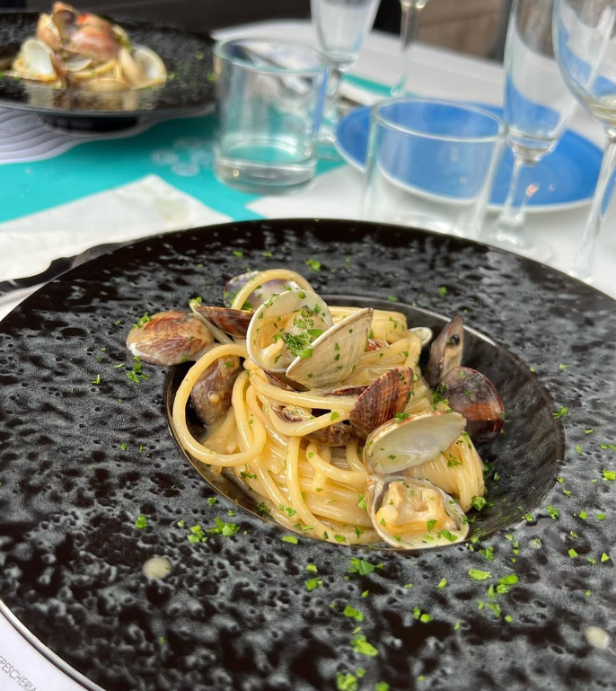 Spaghetti alle vongole serviti su un piatto nero strutturato, guarniti con prezzemolo.