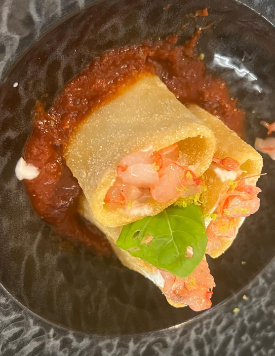 Involtini di pasta ripieni di gamberi con salsa di pomodoro e basilico su un piatto scuro.