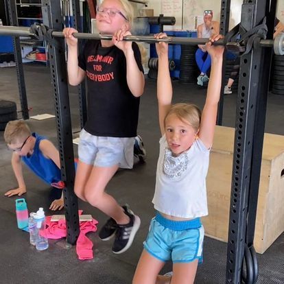 Young girl and boy practicing pull-ups at a Kansas Strength and Performance gym, encouraging youth fitness and activity.