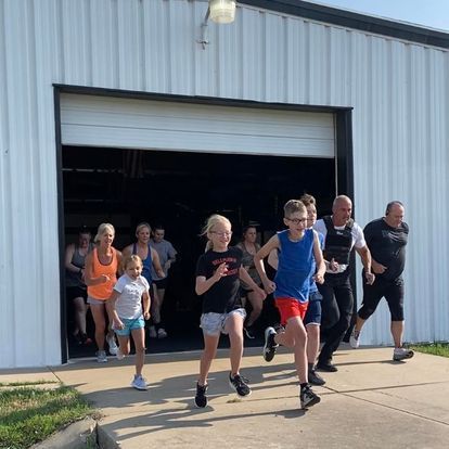 Children and adults energetically sprinting out of a Kansas Strength and Performance gym during a community fitness event.