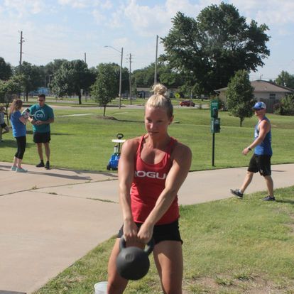 Woman outdoors pulling a sled loaded with weights, showing determination and strength in a functional training session.