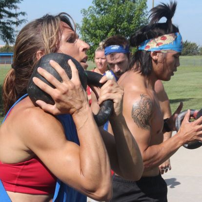 Fitness enthusiast tightly holding a kettlebell close to her chest during an intense outdoor workout session, displaying focus and strength.