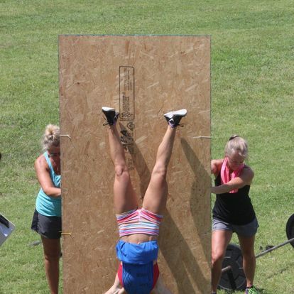 Athlete in action during an outdoor fitness challenge, performing handstand push-ups against a wooden board, demonstrating agility and strength.