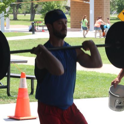 Athletic man lifting a barbell outdoors at a Kansas Strength and Performance event, focusing on strength training under a sunny sky.