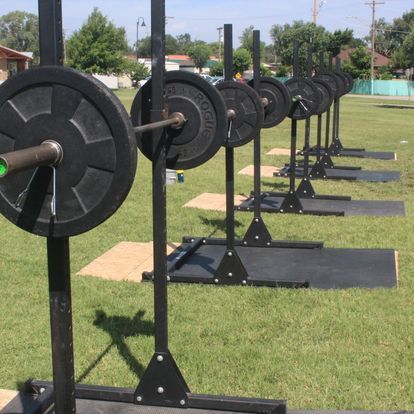 Series of barbell stations set up outdoors on a sunny day for a group fitness event, promoting community and outdoor workouts.