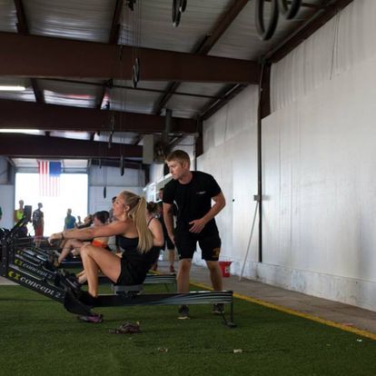 A woman is sitting on a rowing machine while a man stands behind her