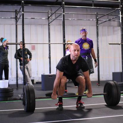 A man is squatting down to lift a barbell in our Gym, Kansas Strength & Performance.